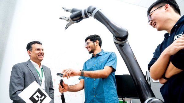 Karunesh Ganguly and graduate students Runfeng Miao and Harsha Peesapati smile as they work with a robotic arm.