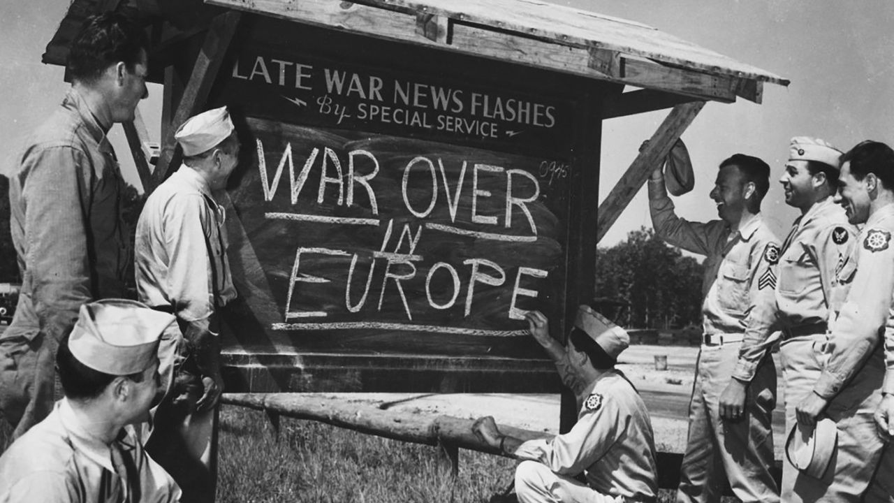 'War over in Europe' written in chalk on a blackboard - surrounded by soldiers in May 1945.