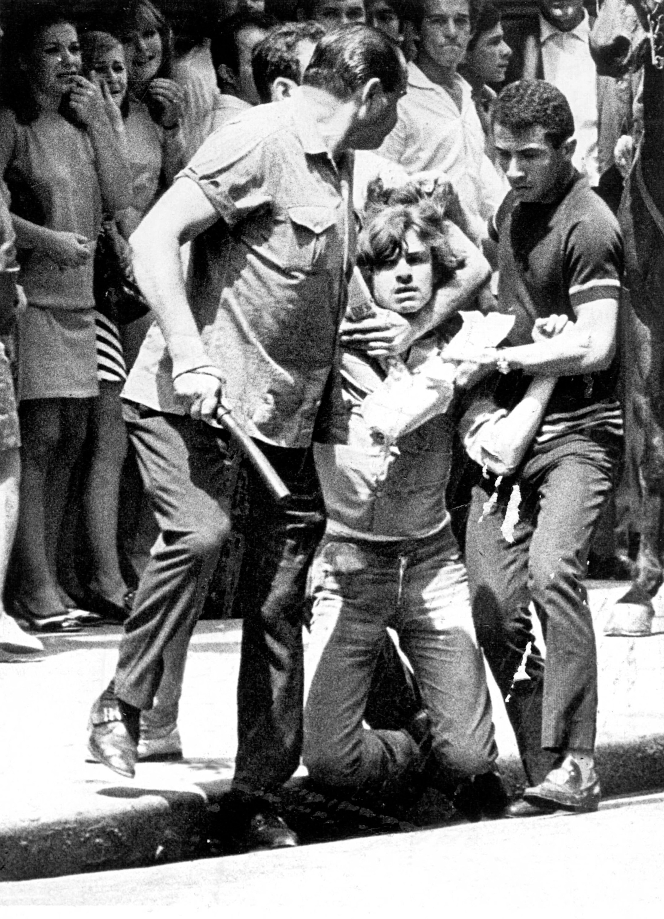 A black and white photograph of a young man being dragged by people derssed in military clothing.