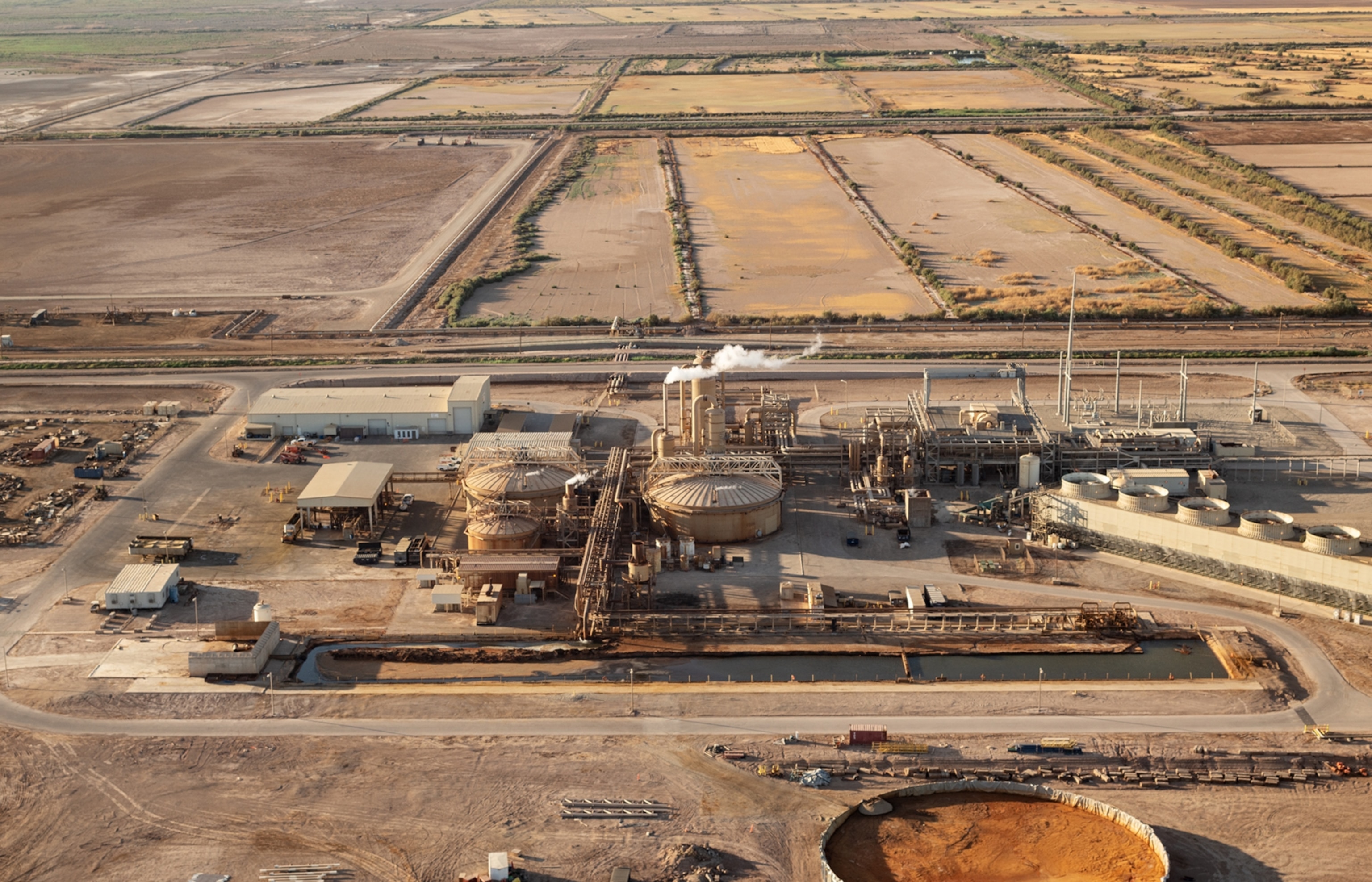 A birds eye view image of a geothermal power plant, which is a round structure that is producing steam. The rest of the location behind and around it is barren and flat.