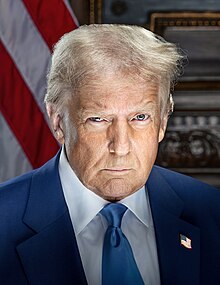 Head-and-shoulders portrait of Trump with a stern facial expression. He is wearing a blue suit, a white shirt, a blue necktie, and an American flag lapel pin. The background is unlit and blurred, and part of an American flag is visible.