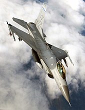 Upright aerial photo of gray jet aircraft flying above clouds