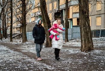 A mother and her two daughters walk past damaged buildings in Kharkiv, Ukraine.