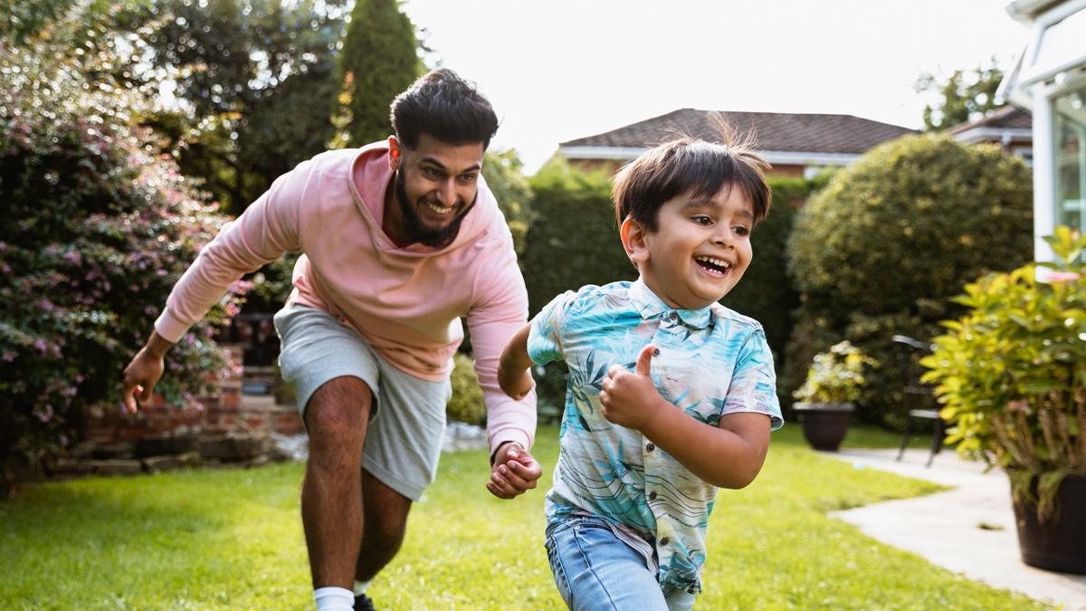 Man plays chase with a young boy in a garden