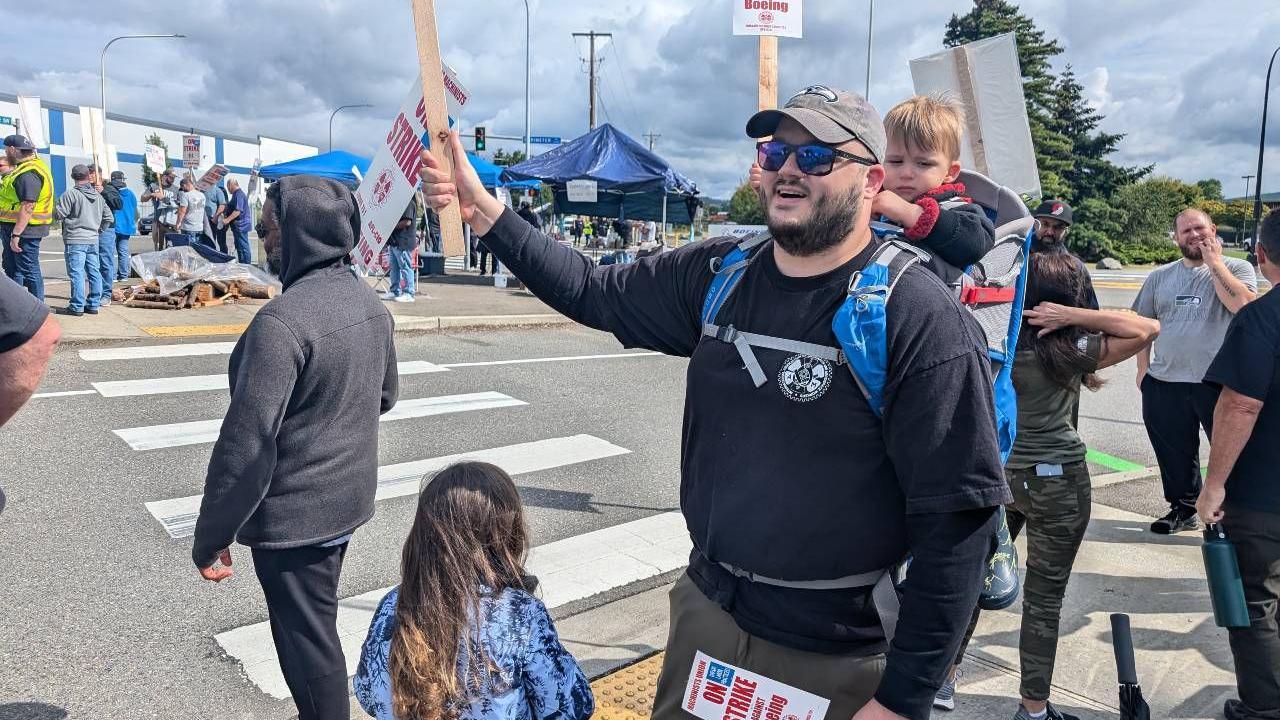 Ryan Roberson attending the protest with his daughter in front of him, her back turned to the camera, and his young son in a carrier on his back