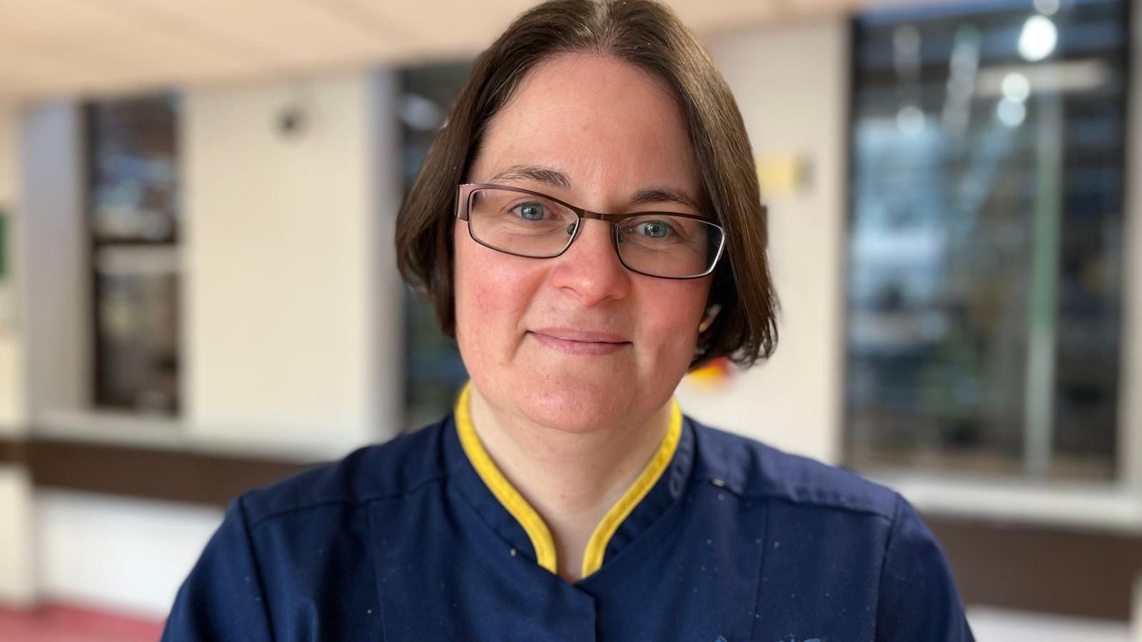 Catherine Theron head of nursing in navy blue scrubs with short brown hair smiles at the camera