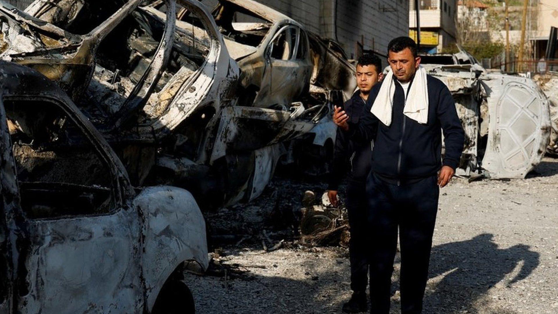 Palestinians walk near cars burned in an attack by Israeli settlers near Hawara in the occupied West Bank (27 February 2023)