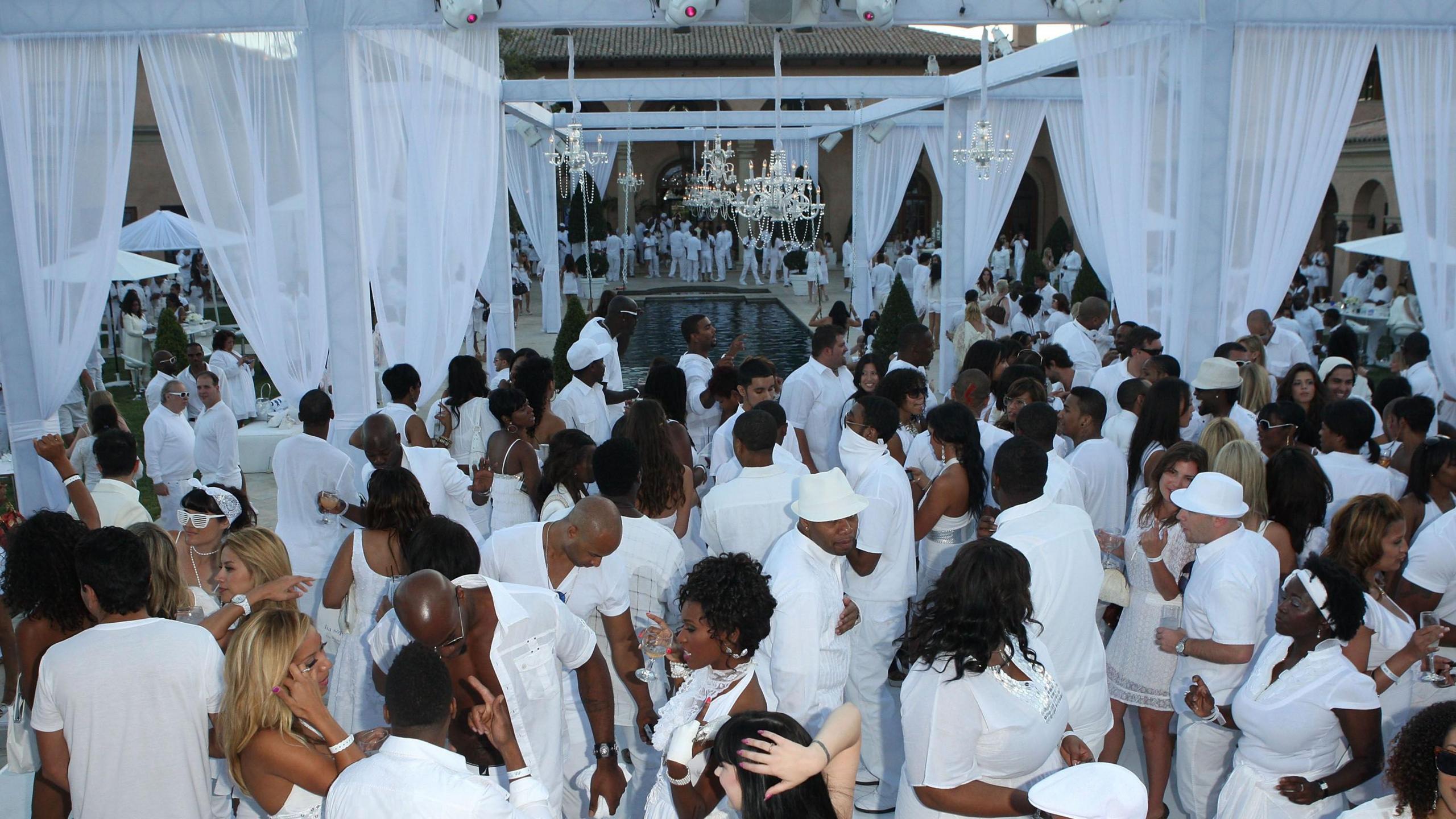 Dozens of people dressed in all-white gather around a pool with diamond chandeliers and white sheer curtains at Sean "Diddy" Combs' White Party in 2007 