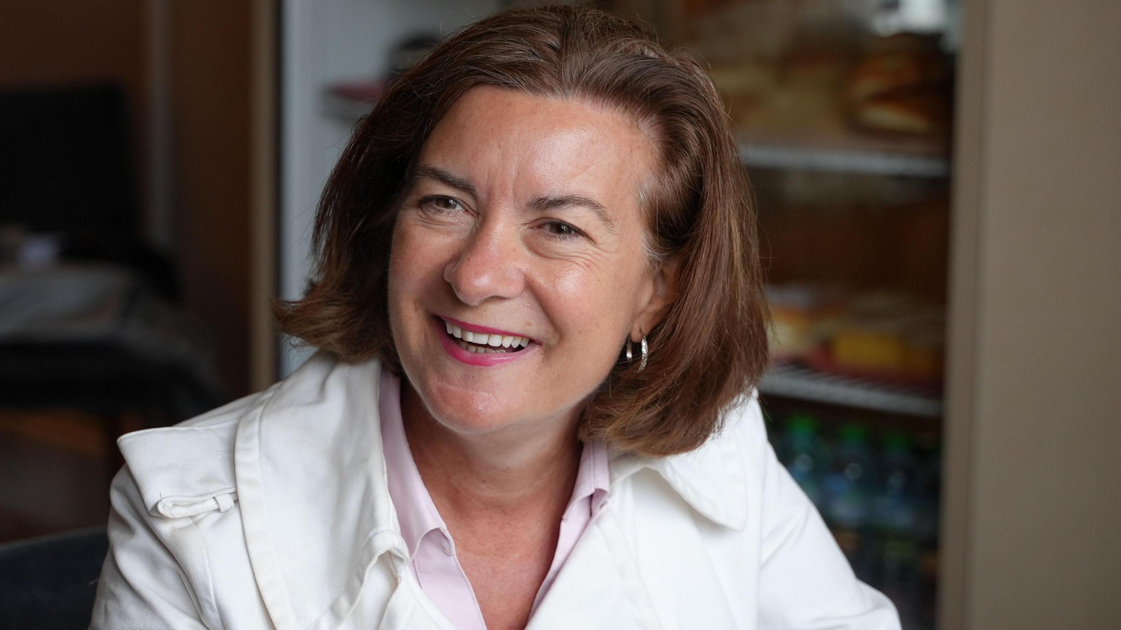 Eluned Morgan wearing a white jacket sat in front of a fridge.