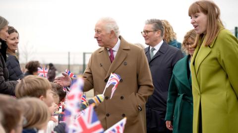 The King, Prime Minister and Deputy Prime Minister on a visit together in Cornwall - children are waving Union flags and the trio are smiling and speaking with the crowd