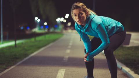 A woman out jogging at night and pausing for a rest 