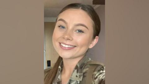 Jaysley Beck in green Army clothes smiling with her hair tied back. She has blue eyes and brown hair.