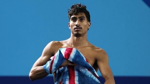 Kyle with a Team GB towel, after coming out from the water. The background is blue.