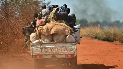 A pick-up truck transporting people and goods drives past burning fields as it heads to Wau on January 31, 2020. 