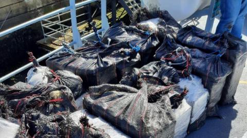 Blocks of drugs wrapped in black sacking material on board a boat deck