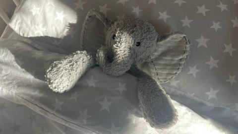 Toy elephant lies on a pillow in bed, tucked up under duvet