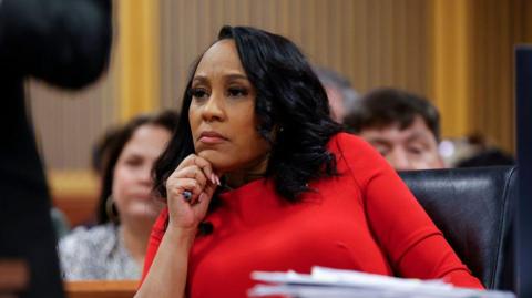 Fani Willis sits in court wearing a red dress.