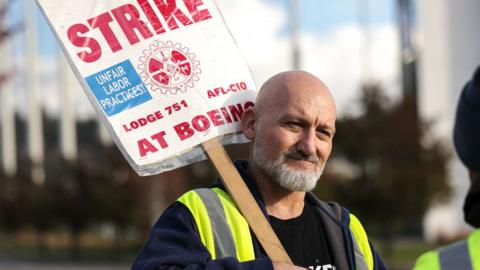 A Boeing machinist stands with a placard whilst striking in Renton, Washington, on 3 November 2024