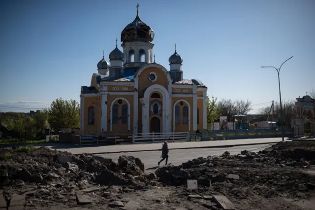 A woman walks by the damaged St. Godmothers Cover Church, on May 4, 2022 in Malyn, Ukraine.