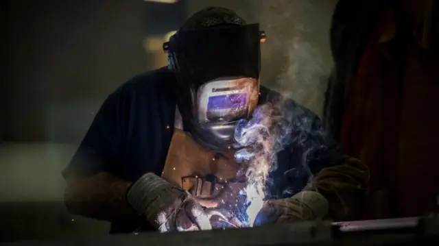 A metal worker with sparks in front of their visor