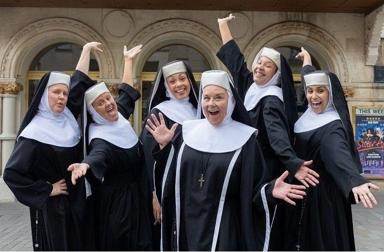 The cast of Sister Act, dressed as nuns, stand in a theatrical pose outside the Theatre Royal in Bath