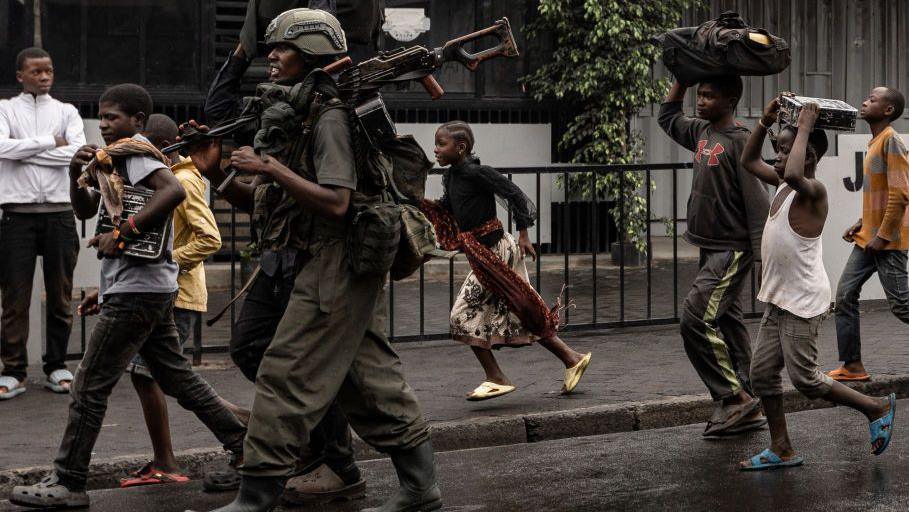 A member of the M23 armed group walk alongside residents through a street of the Keshero neighbourhood in Goma, on January 27, 2025. 