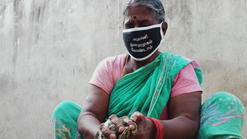 A woman washes dishes as she wears a mask to protest port expansion