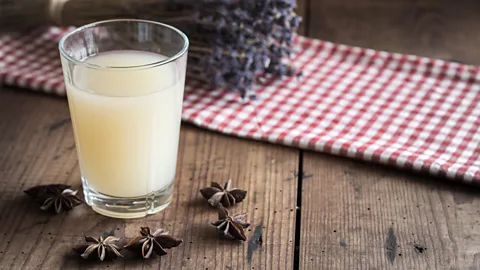 A glass of pastis on a table surrounded by star anise and a cloth with a bushel of lavender in the background (Credit: Alamy)