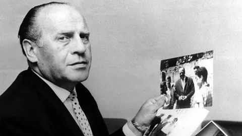 Oskar Schindler holds up a photograph of him with people (Credit: Alamy)