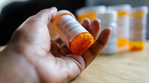 Getty Images A hand holding an ADHD tablet with the pill bottle visible 