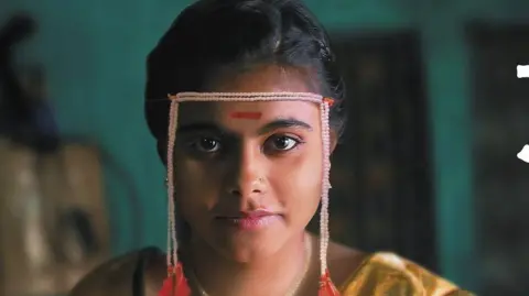 A still from Sthal: A Match shows the lead character played by Nandini Chikte  sitting on a wooden stool 