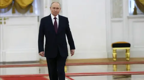 Putin walking along a white painted corridor with gold stools and curtain in the background.