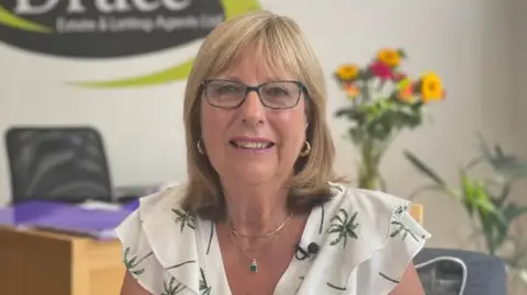 Linda Druce from Druce Estate & Letting Agents sitting in her office smiling into the camera 