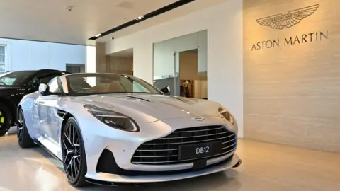 Getty Images A silver Aston Martin DB12 parked in a sales garage.