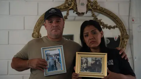 A man and a woman are seen holding photos of their dead son