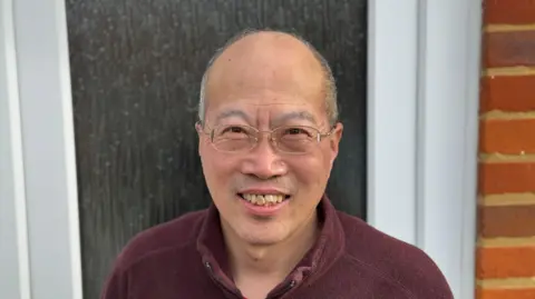 George King/BBC Wenge Yuan standing in front of his front door while smiling into the camera