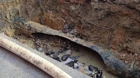 Burst pipe underneath road covered in mud and water