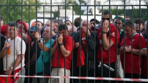 PA Media Liverpool fans queue outside the Stade de France in Paris ahead of the 2022 Champions League final. They are standing behind high metal fences.