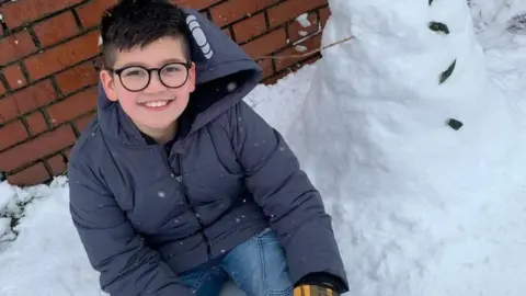 Family Twelve-year-old Azaan Khan sits next to a snowman.