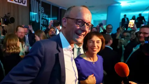 Reuters Friedrich Merz and his wife Charlotte talk to journalists