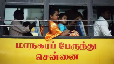 Getty Images A yellow and black coloured bus in southern India's Chennai city, with a woman in sari seen with a child in her lap