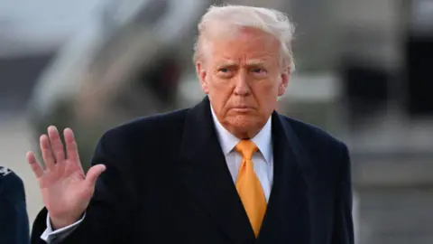 US President Donald Trump in a black overcoat and suit waves to reporters as he walks outside