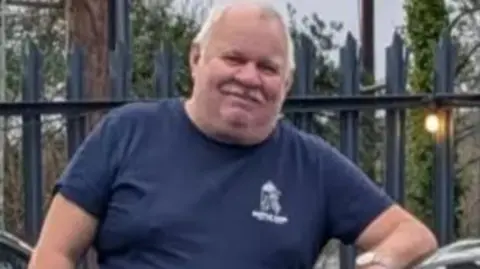 Man with moustache and wearing a dark T-shirt looks at the camera