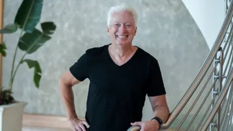 Alan Lafley Former P&G CEO Alan Lafley poses in a black t-shirt whilst standing at the bottom of a stair case with a silver metal railing 