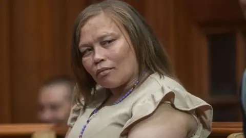 Kelly Smith, dressed in a beige dress and wearing a purple necklace, looks on during court proceedings in her human trafficking case