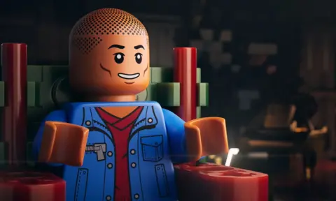 Focus Features Pharrell Williams, as a Lego minifigure, being interviewed for the documentary Piece By Piece. He is wearing a blue denim jacket.