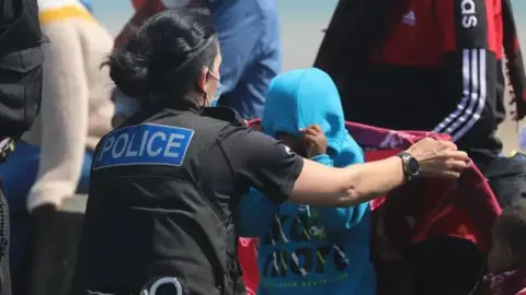 A police officer with a child who is getting off a boat, wearing a blue jacket with the hood over their head