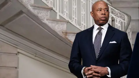 Getty Images Eric Adams - a bald man - looks to the side, off camera. He is wearing a suit and there is a staircase behind him