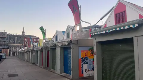 Norwich markets. A row of market stalls with coloured shutters which are closed.