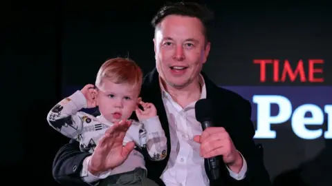 Getty Images NEW YORK, NEW YORK - DECEMBER 13: Elon Musk and son X Æ A-12 on stage TIME Person of the Year on December 13, 2021 in New York City. (Photo by Theo Wargo/Getty Images for TIME)